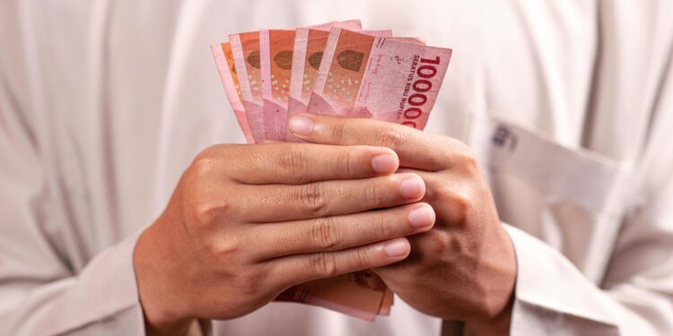 Close-up of hands holding 100,000 Indonesian Rupiah notes, symbolizing wealth and finance.