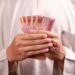 Close-up of hands holding 100,000 Indonesian Rupiah notes, symbolizing wealth and finance.