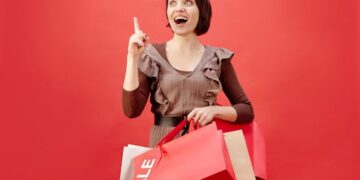 Cheerful woman with shopping bags celebrating a sale on a vibrant red backdrop.