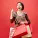 Cheerful woman with shopping bags celebrating a sale on a vibrant red backdrop.