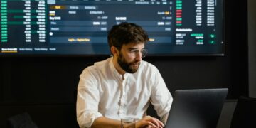 Professional analyzing stock market trends using laptop and digital display in modern office.