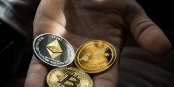 Hand holding Bitcoin, Ethereum, and Ripple coins representing digital currency.