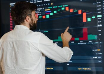 A man analyzes cryptocurrency graphs on a touchscreen monitor in a modern office setting.