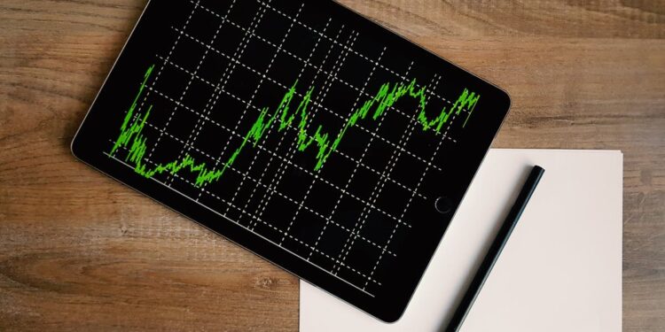 Flatlay of an iPad displaying stock market graph on a wooden desk with a pencil and paper.