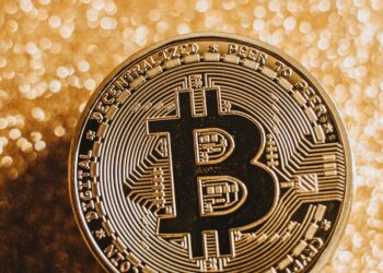 A close-up of a Bitcoin coin against a shimmering gold background, symbolizing digital currency and finance.