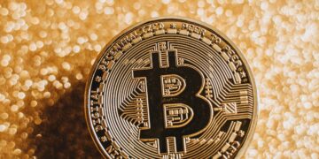 A close-up of a Bitcoin coin against a shimmering gold background, symbolizing digital currency and finance.