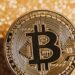 A close-up of a Bitcoin coin against a shimmering gold background, symbolizing digital currency and finance.