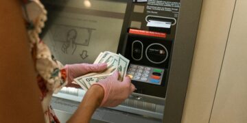 A person wearing gloves withdraws cash from an ATM, ensuring hygiene.